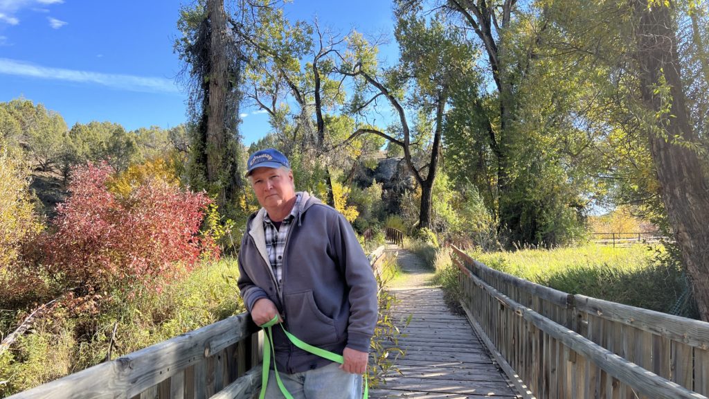 Elgin Cook stands on a bridge with fall colors behind him