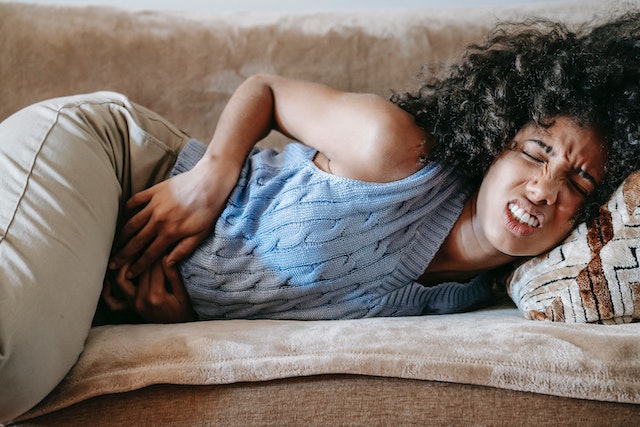 Woman holding stomach while laying on a couch sick